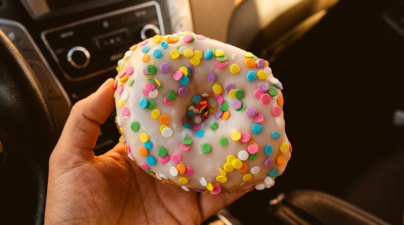A hand holds a white-frosted donut with colorful sprinkles inside a car.