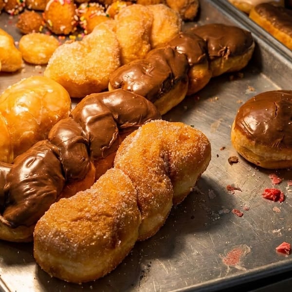 A metal tray filled with various donuts, including glazed, chocolate, sugar-dusted, and donut holes.