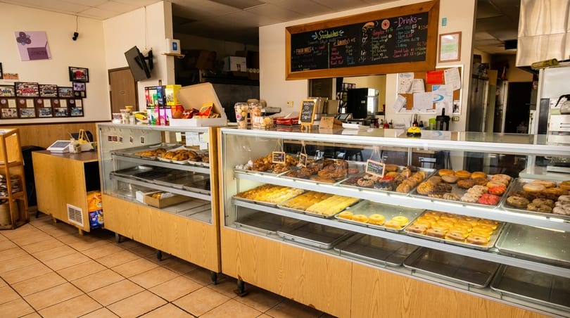 A brightly lit donut shop interior with display cases full of various pastries and donuts.